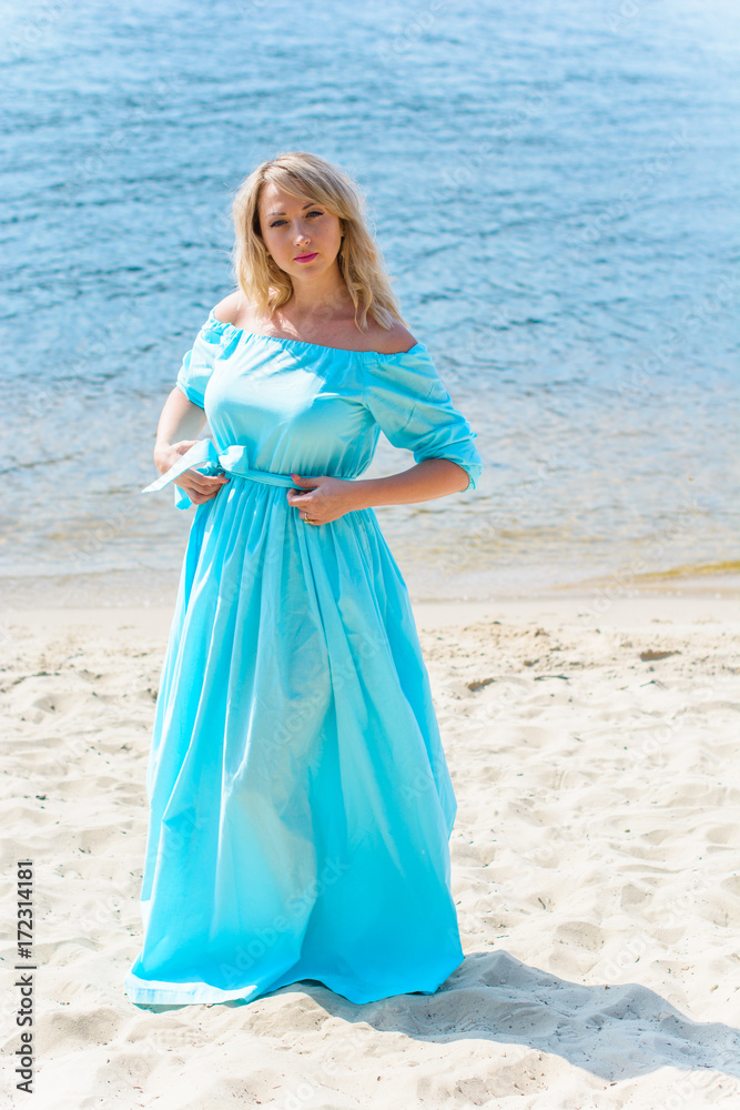 Nice woman in blue long dress walk on a beach and relax at warm day. Tenderness plus size blonde hair lady look stylish and sweet Nice woman in blue long dress walk on a beach and relax at warm day. Tenderness plus size blonde hair lady look stylish and sweet