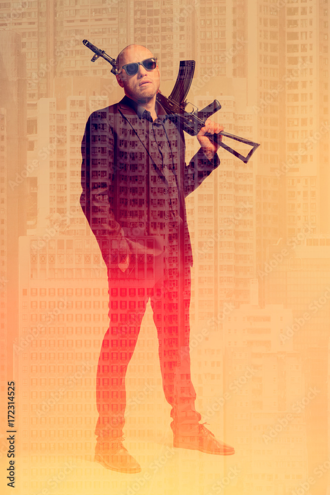 Bald man in a gray suit and sunglasses holding a machine gun on his shoulder against the backdrop of the city. Toned Bald man in a gray suit and sunglasses holding a machine gun on his shoulder against the backdrop of the city. Toned