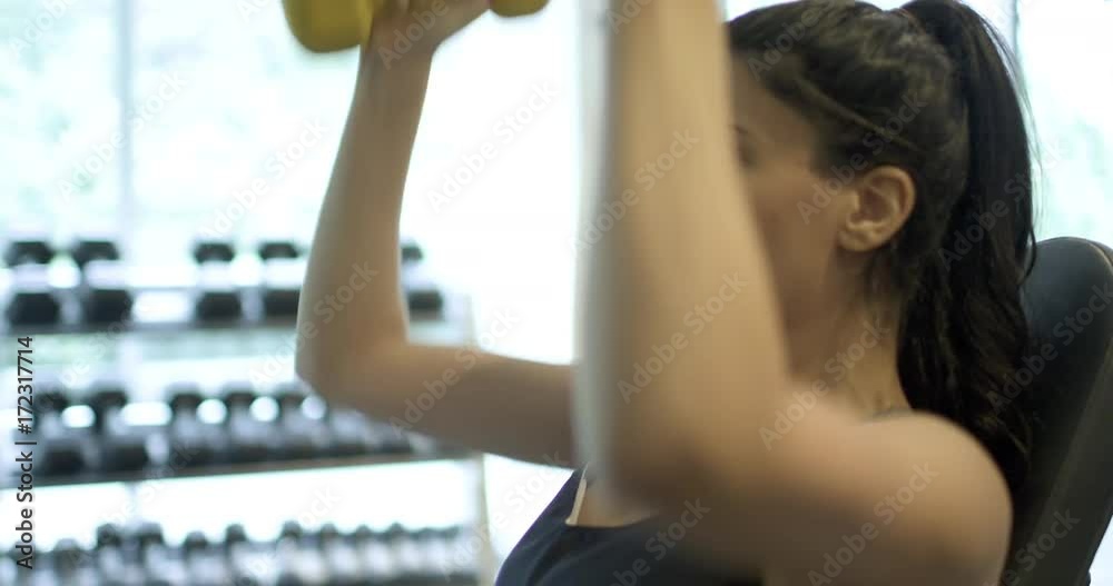 Beautiful woman does a military press with small weights