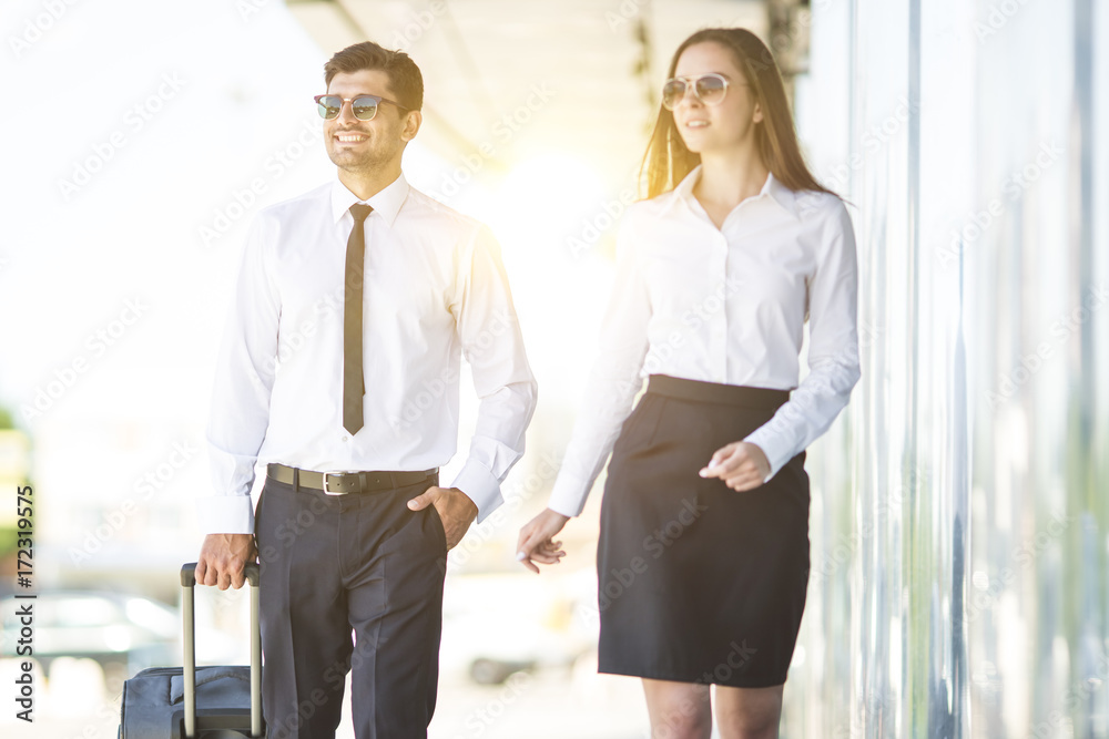 Fototapeta premium The business man and woman in sunglasses walk with a suitcase