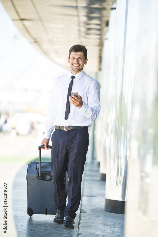 The happy businessman phone and walk with a suitcase near building The happy businessman phone and walk with a suitcase near building