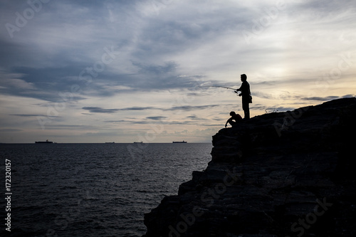 Silhouette of fisherman on cliff