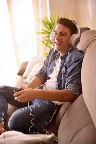 Teenager laughing with smartphone and headphones on couch vertical composition