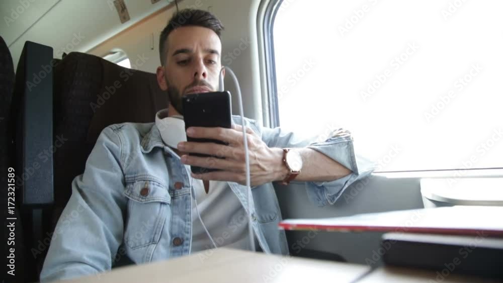 Ragazzo sta viaggiando su un treno mentre ascolta musica dalle cuffie e usa lo smart phone.