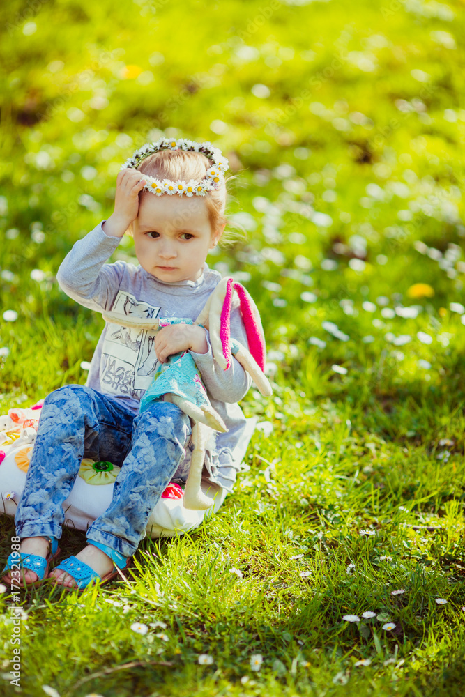 Girl with toy and flowers sits on the green lawn