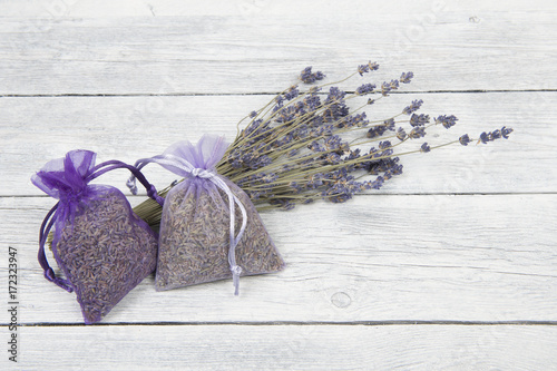 Two lavender sachets and a bunch of dried lavender flowers on a white wooden planks background