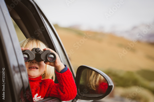 little girl looking through binoculars travel by car in mountains