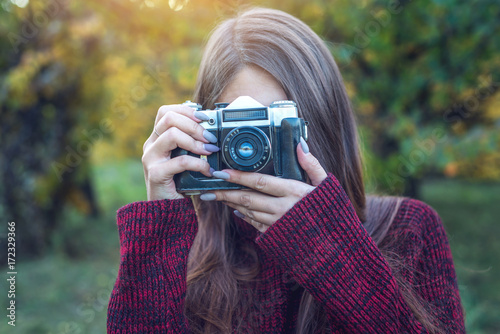 Beautiful woman in autumn Park holds vintage retro camera. Concept of photography as a hobby