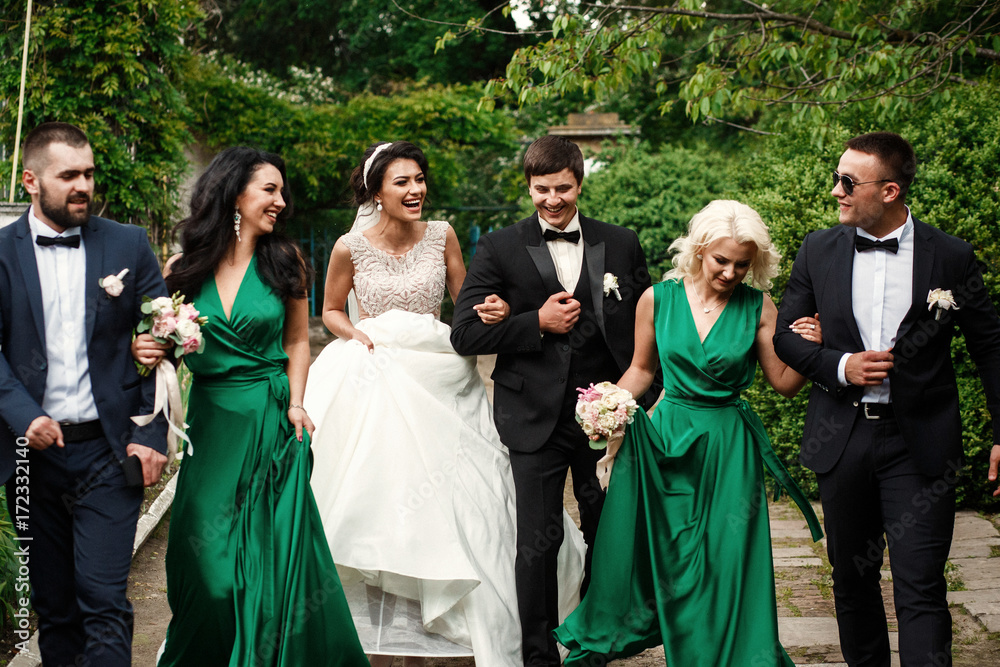 Newlyweds and their smiling friends walk across the garden