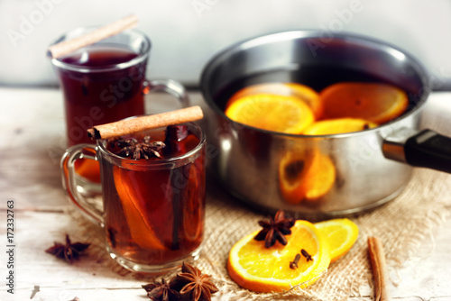 mulled wine in a glass mugs and in a pot with Christmas spices like orange slices, cloves, star anise and cinnamon on a bright rustic wooden tabled