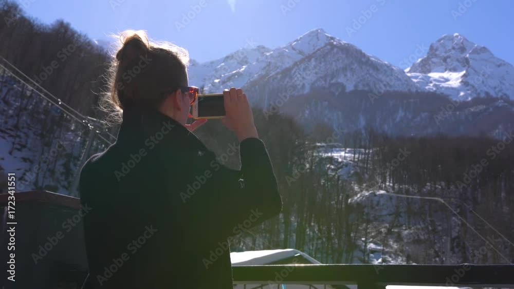 Young woman makes photo of scenic mountains with cellphone. Krasnaya Polyana, the Caucasus, Russia