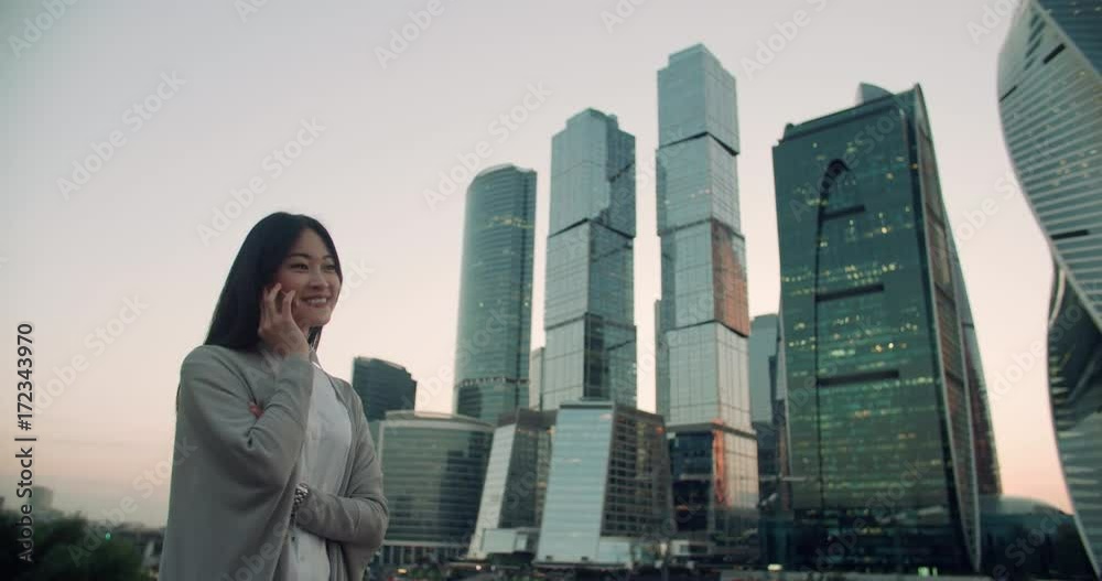 young successful Asian business woman portrait, woman talking on the phone in the background of a skyscraper, close-up young successful Asian business woman portrait, woman talking on the phone in the background of a skyscraper, close-up