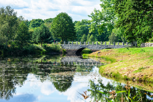 Old stone bridge with arches spanning across narrow river in woodland landscape. Location Vissefjarda in southern Sweden.