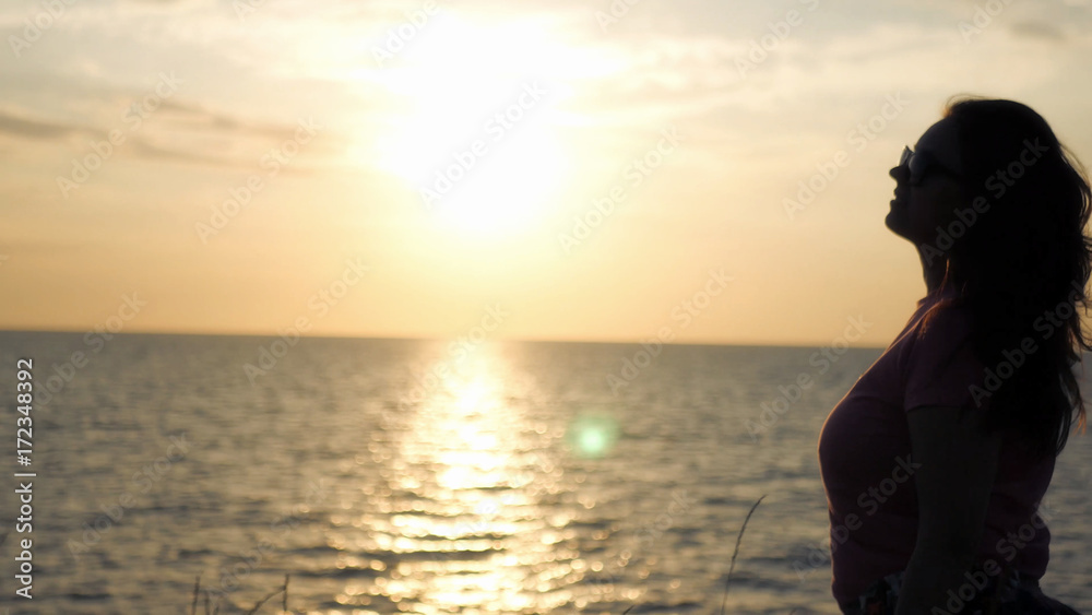 A young girl admires the beautiful sunset by the sea, a light wind blows.
