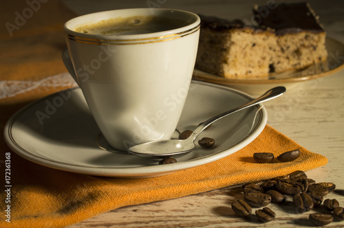 Coffee in a white cup. Spilled coffee beans. Sweet dessert on a plate of coffee. In the dark with side light and analog effect in retro - vintage style photo