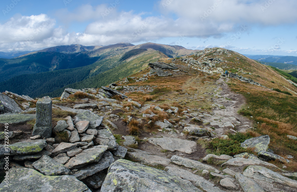 Fototapeta premium Hiker walks the stony road on the mountain ridge with a former Polish-Czechoslovak border column in the foreground