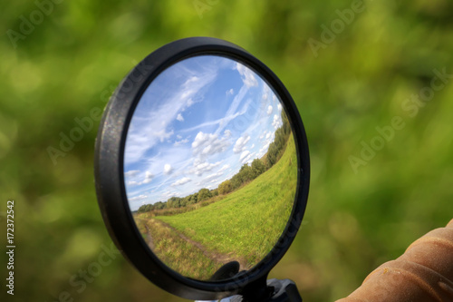 rural landscape with blue sky and field is reflected in the mirror of the bike