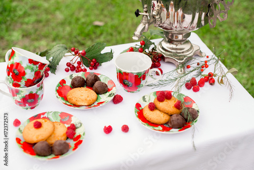 Самовар с чашками и десертом с малиной на столе в саду. Завтрак на природе 