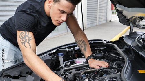Handsome young man trying to repair a car engine, looking inside open bonnet