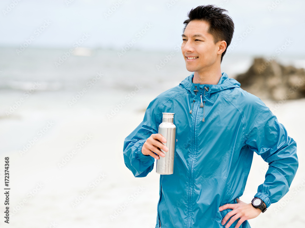 Young man in sport clothes drinking water after workout on the beach Young man in sport clothes drinking water after workout on the beach