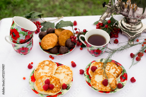 Самовар с чашками чая и десертом с малиной на столе в саду