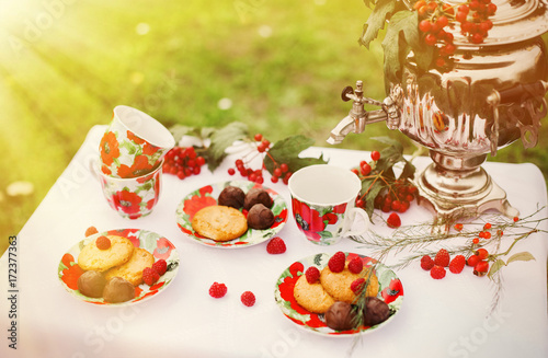 Утренний завтрак в саду. Самовар, блюдца, чашки стоят на столе. Печенье, конфеты, малина на завтрак