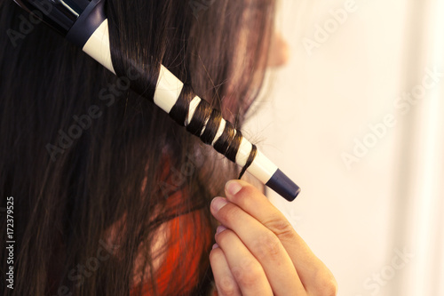 Hairstylist curling hair client in hairdressing salon