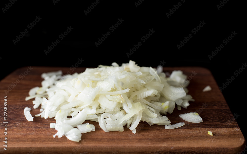 Finely chopped onion on a wooden board on a black background, closeup Finely chopped onion on a wooden board on a black background, closeup