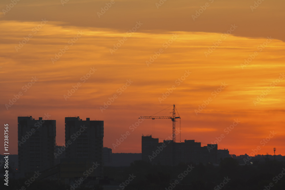 Construction cranes near residential apartments - view on sunrise, horizontal