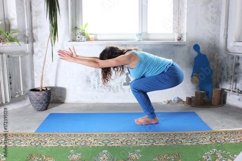 Young attractive smiling woman practicing yoga, sitting in One Legged King Pigeon exercise, Eka Pada Rajakapotasana pose, working out, wearing sportswear, grey pants, bra, indoor full length, home photo