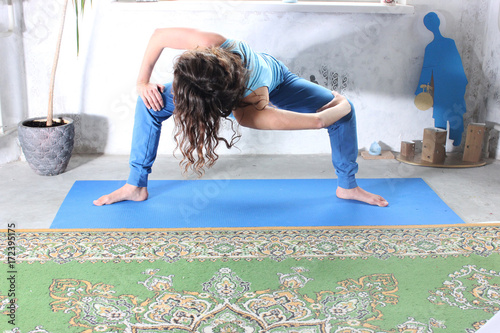 Young attractive smiling woman practicing yoga, sitting in One Legged King Pigeon exercise, Eka Pada Rajakapotasana pose, working out, wearing sportswear, grey pants, bra, indoor full length, home photo