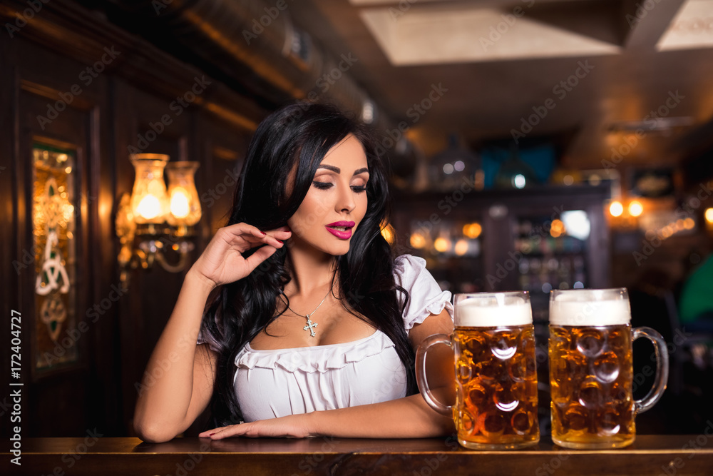 Oktoberfest. Brunette woman holding beer mugs in bar Oktoberfest. Brunette woman holding beer mugs in bar