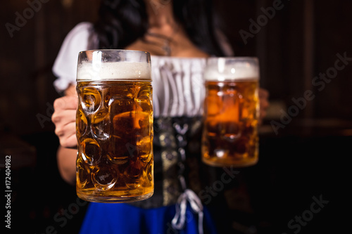 Young sexy Oktoberfest waitress, wearing a traditional Bavarian dress, serving big beer mugs at bar.