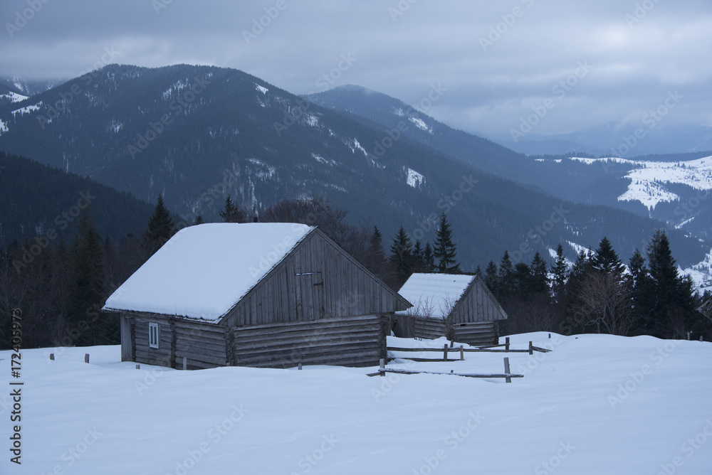 Old wooden houses and fence with snowy mountains in winter, Carpathians, Ukraine 