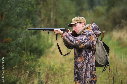 Hunter with a backpack and a hunting gun in the autumn forest. The man is on the hunt. Hunter is aiming.