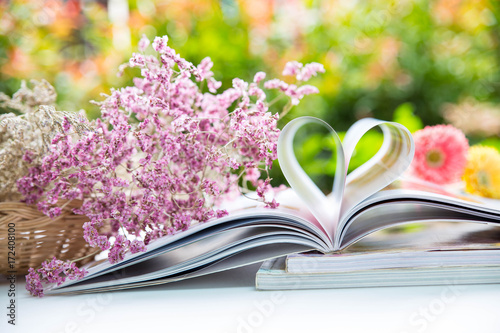 Book with heart shape of paper and there are dry flowers in rattan basket , colorful nature background and bokeh