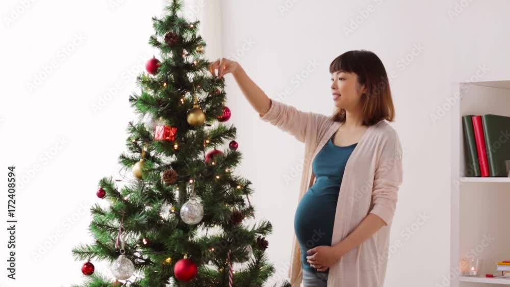 pregnant woman decorating christmas tree at home pregnant woman decorating christmas tree at home