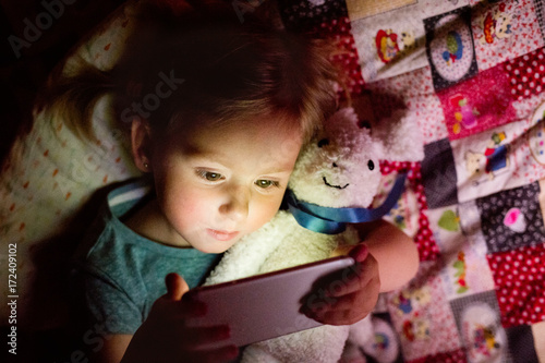 Little girl at home at night watching something on smartphone.