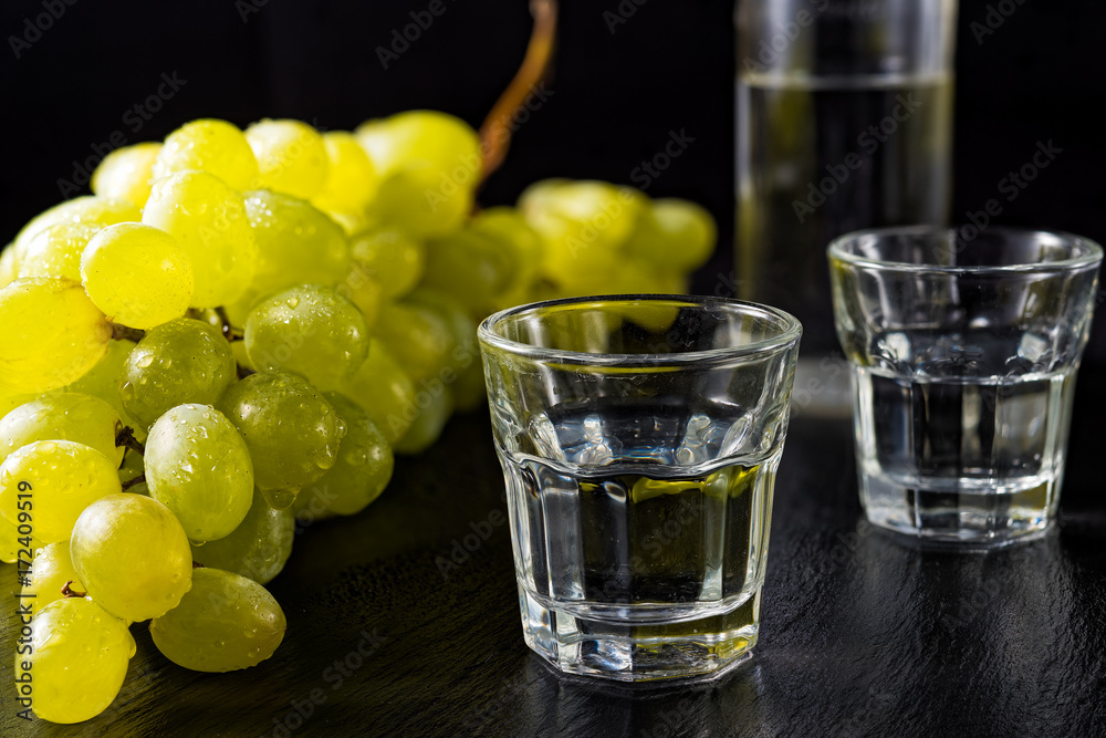 Two glasses and bottle of traditional drink Ouzo or Raki on black dish with a branch of grapes Two glasses and bottle of traditional drink Ouzo or Raki on black dish with a branch of grapes
