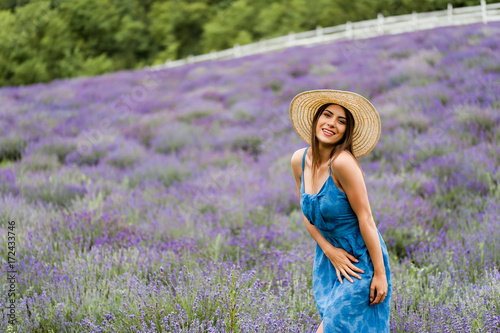 Portrait of sitting woman in the field of blossoming lavender looking at camera and smiling