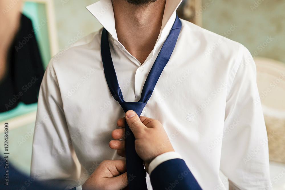 Φωτογραφία Groom's friend helps to fix a blue tie on groom's neck while they stand in the r