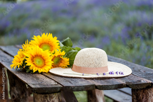 Fototapeta Naklejka Na Ścianę i Meble -  Sunflower bouquet and a straw hat on a wood table at the sunset, over lavender field background.