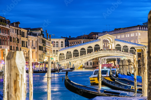 Venice, Italy. Rialto bridge and Grand Canal at twilight blue hour. Gondolas on the foreground. Tourism and travel concept.