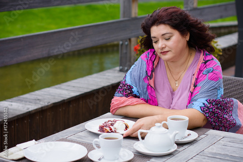 Plump nice american middle age simple woman sit in cafe on a terrace at warm autumn day and enjoy the life, have cozy mood