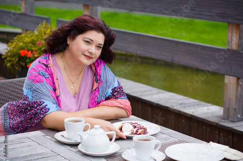 Plump nice american middle age simple woman sit in cafe on a terrace at warm autumn day and enjoy the life, have cozy mood