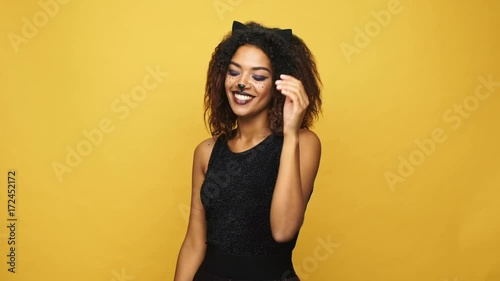 Funny lady with cat make up and wearing black dress scaring you and smiling isolated over yellow 
 photo