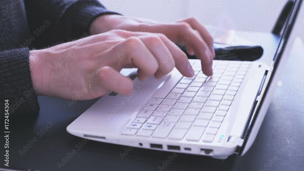 A man (Man's hands), an office worker, sits at home outside his time using a laptop and a bank credit card, pays for online payment in an online store. A man (Man's hands), an office worker, sits at home outside his time using a laptop and a bank credit card, pays for online payment in an online store.