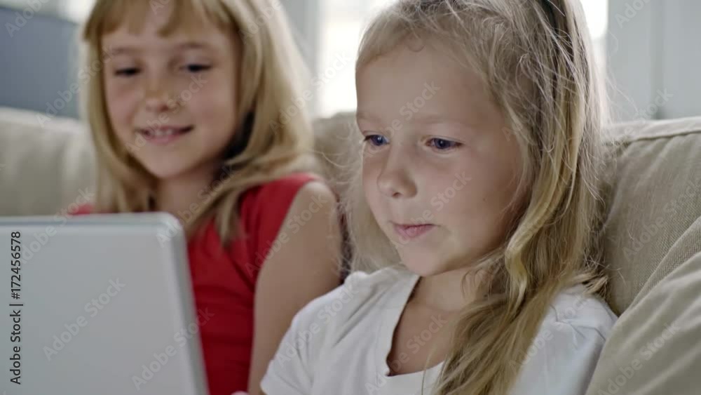 Medium shot of laughing little girls with blond hair laughing and taking pictures on tablet Medium shot of laughing little girls with blond hair laughing and taking pictures on tablet