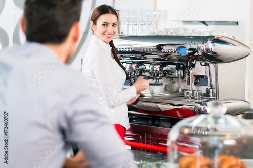 Attractive waitress smiling to male customer while preparing espresso at the automatic coffee machine indoors