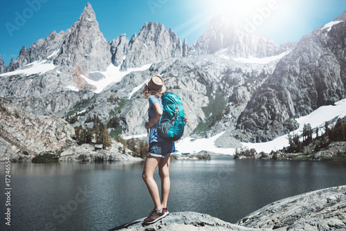 Young traveler woman hiking in the stunning mountain wilderness, standing in front of amazing cold lake